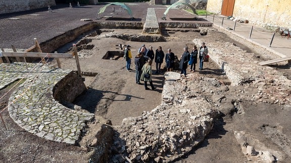 Eine kleine Gruppe Menschen steht 2022 auf den ausgegrabenen Mauerresten einer großen Kirche in der Sonne.