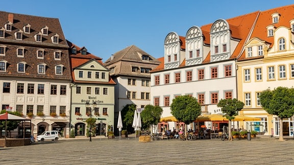 Auf dem Marktplatz von Naumburg im Burgenlandkreis sind mehrere Cafés und Restaurants in historisch anmutenden Gebäuden zu sehen. 