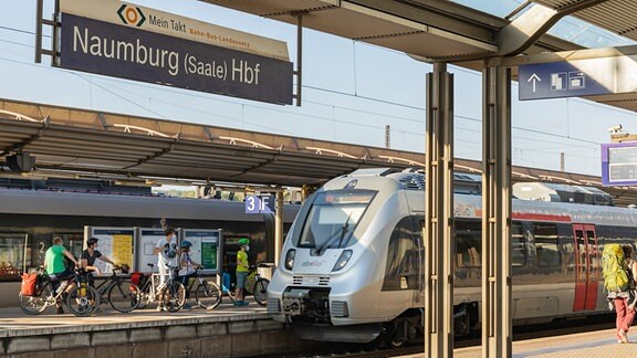 Im Bahnhof von Naumburg steht ein Abellio-Zug an einem Bahnsteigt. Im Hintergrund laufen Menschen mit Fahrrädern. 