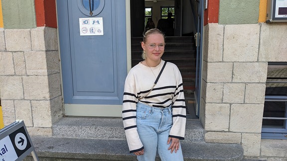 Eine junge Frau mit blonden Haaren steht vor einem Wahllokal in Naumburg