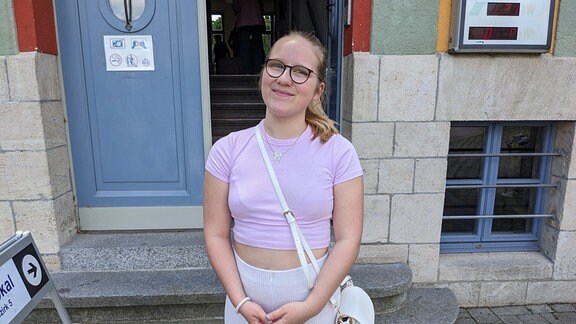 Eine junge Frau mit Brille und blonden Haaren steht vor einem Wahllokal in Naumburg