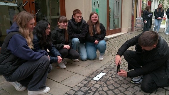 Ein Mann fotografiert Jugendliche mit im Boden verlegten Gedenksteinen an deportierte Juden.