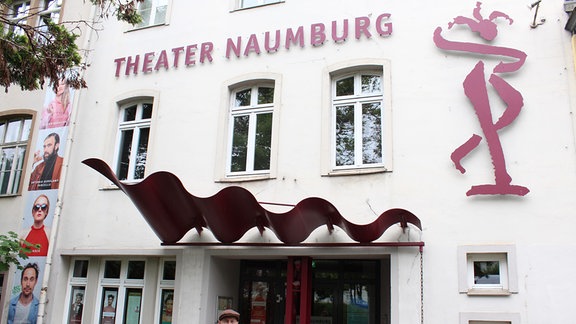 Intendant Stefan Neugebauer steht vor dem Eingang des Theaters in Naumburg, über dessen Eingang eine geschwungene Skulptur zu sehen ist. 