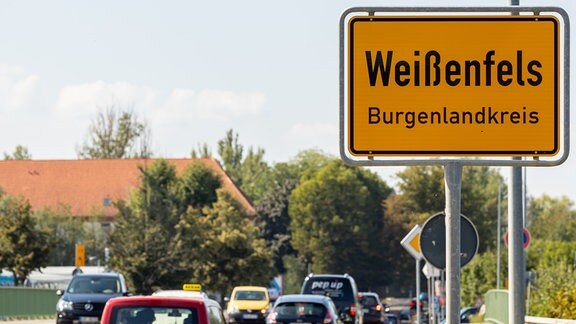 Neben einer von Autos befahrenen Straße steht das Ortseingangsschild von Weißenfels. 