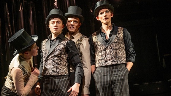 Vier Personen in gestreiften Hosen, mit Weste und Zylinder auf einer Theaterbühne