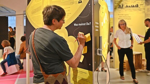 Eine Besucherin schreibt etwas auf eine interaktive Tafel in einem Ausstellungsraum.