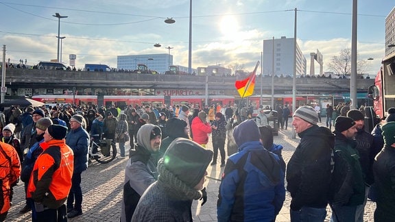 Viele Menschen stehen am Riebeckplatz in Halle, einer hält eine Deutschland-Fahne.