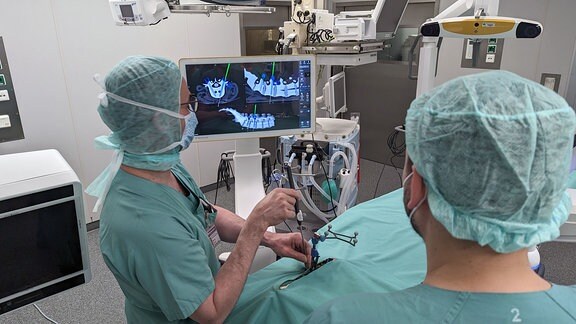 Zwei Ärzte während OP mit Unterstützung eines Roboterarms.