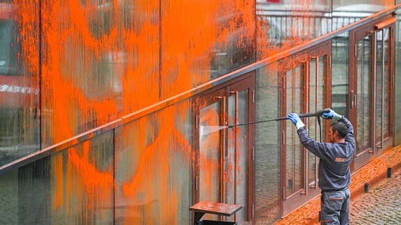 Mit einem Hochdruckreiniger entfernt ein Mitarbeiter einer Spezialfirma die orangene Farbe von der Glasfassade.