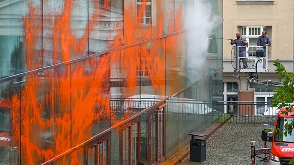 Mitarbeiter einer Spezialfirma entfernen die orangene Farbe von der Glasfassade.