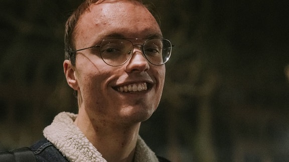 Ein junger Mann mit Brille lächelt in die Kamera