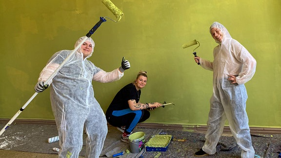 Drei Menschen streichen eine Wand gelbgrün an.