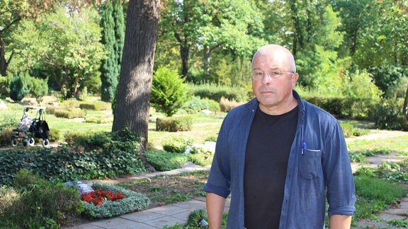 Andreas Herzig, ein älterer Mann mit kurzen weißen Haaren und blauer Jeansjacke, steht auf den Südfriedhof in Halle.