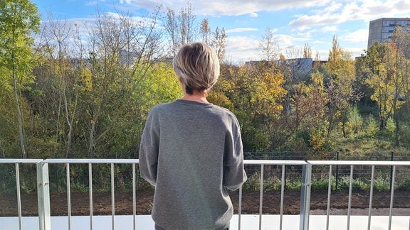Eine Frau steht auf einem Balkon und schaut in die Natur.