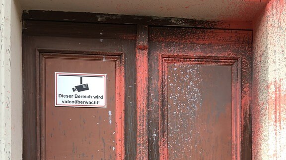 Eine mit roter Farbe beschmierte Haustür mit einem Schild, dass auf videoüberwachung hinweist.
