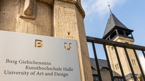 Vor dem Eingangsportal der Kunsthochschule Burg Giebichenstein in Halle hängt eine Informationstafel.