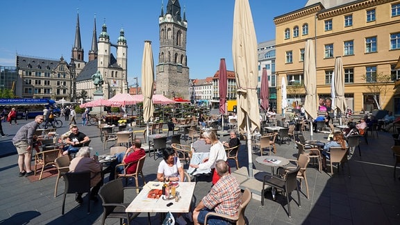 Gäste sitzen in einem geöffneten Freisitz in der Innenstadt von Halle bei frühsommerlichen Temperaturen und Sonnenschein.