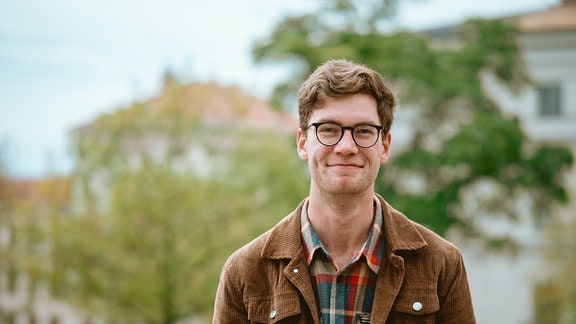 Jan Niklas Reiche, ein junger Mann mit Brille, lächelt in die Kamera