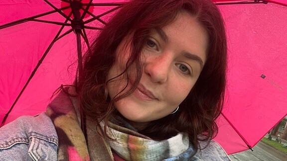 Eine junge Frau mit pinkem Regenschirm lächelt in die Kamera