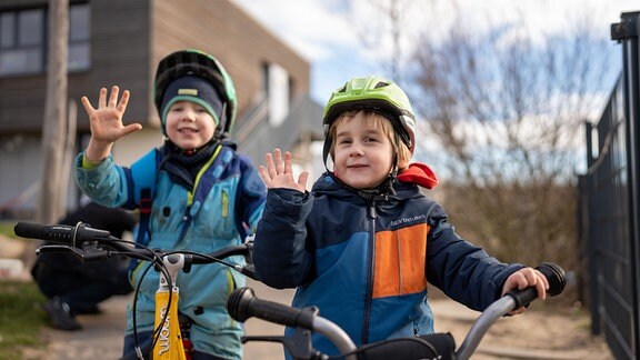 Zwei Kinder mit kleinen Fahrrädern und Helmen.