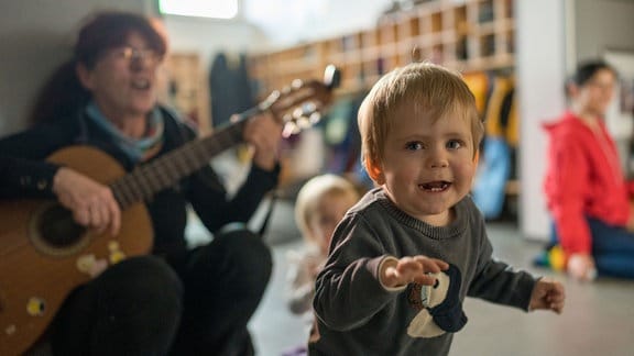 Eine Frau spielt Gitarre neben einem lachenden Kind.