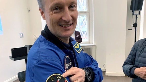 Astronaut Matthias Maurer zeigt auf des Emblem der Mission auf seinem Anzug.
