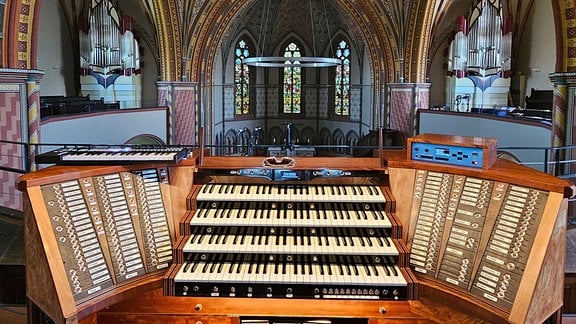 Das Pult einer modernen Orgel mit 4 Spielebenen und zwei Registertafen mit Blick in das Kirchenschiff  
