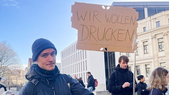 Ein junger Mann hält ein Portestschild hoch auf dem steht: "Wir wollen drucken"