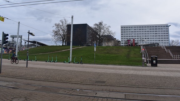 Blick auf eine Wiese auf einer Anhöhe am Riebeckplatz in Halle. Im Hintergrund sind mehrere hohe Gebäude.