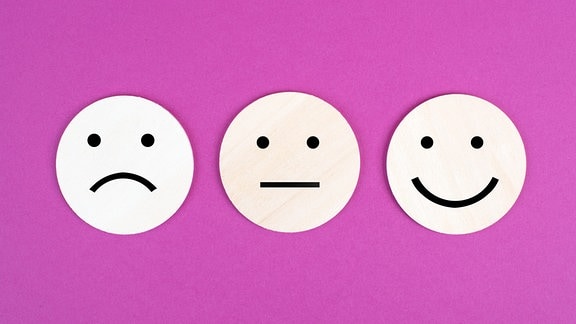 Drei Gesichter, lächelnd, traurig in verschiedenen Farben auf rosa Hintergrund