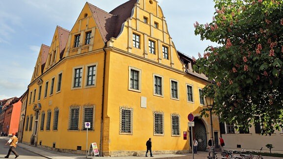 Passant*innen vor einem alten Haus mit gelber Fassade