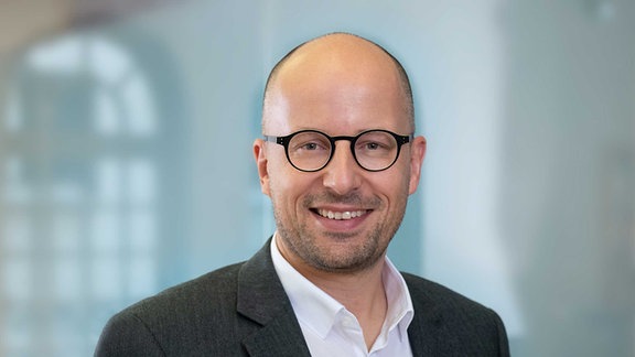 Steffen Müller, ein Mann mit schwarzer Brille und Glatze, lächelt in die Kamera