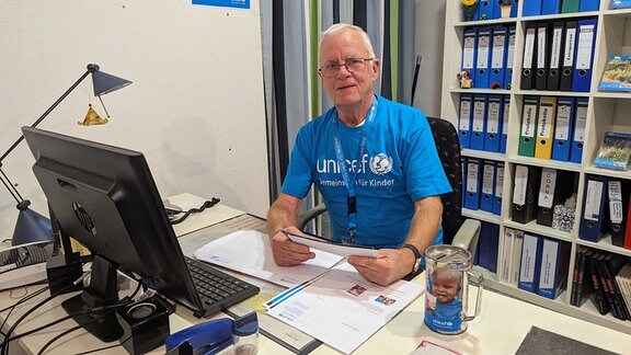 Eine Person mit Unicef T-Shirt sitzt an einem Schreibtisch.