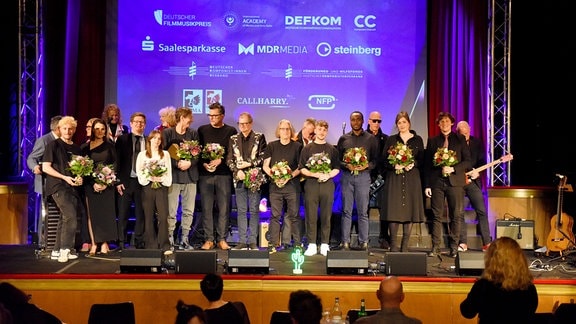 Ein Gruppenbild der Gewinnerinnen und Gewinner des Deutschen Filmmusikpreises 2023, alle stehen auf der Bühne und haben einen Blumenstrauß in der Hand.