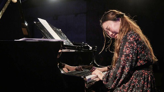 Eine Frau spielt expressiv vertieft Piano.