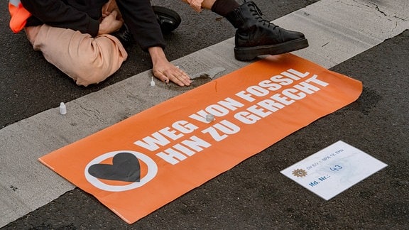 Ein Aktivist der Klimaschutz-Gruppe Letzte Generation sitzt auf einer Straße.