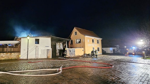 Feuerwehrschläuche liegen über eine nasse Straße in Ummendorf verteilt.