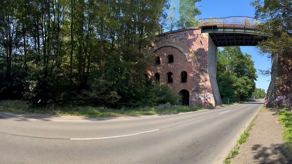 Eine gemauerte Bahnbrücke führt über eine leere Landesstraße