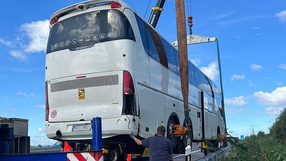 Zwei Schwerlastkräne heben den Reisebus aus dem Straßengraben.