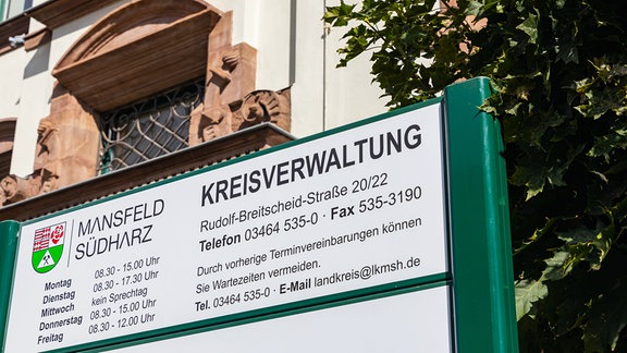 Vor einem historischen Verwaltungsgebäude steht ein Schild, das auf die Kreisverwaltung des Landkreises Mansfeld-Südharz in Sangerhausen hinweist.