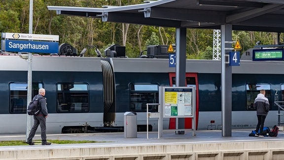 Ein Abellio-Zug steht an einem Gleis im Bahnhof von Sangerhausen, davor laufen Menschen.