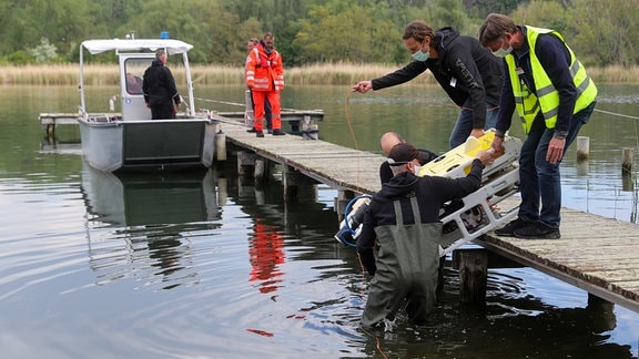 itarbeiter einer Forschungsgruppe heben einen Tauchroboter mit einem hochauflösendem 3D-Laser in den Süßen See.