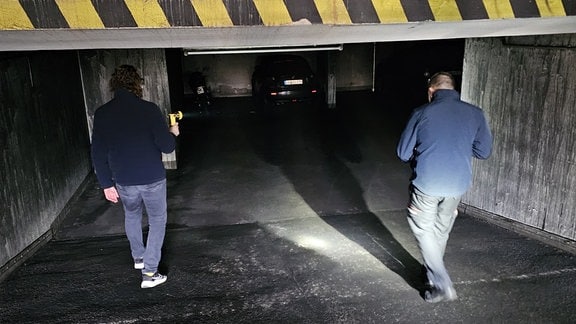 Zwei Männer betreten mit einer Taschenlampe eine Tiefgarage.