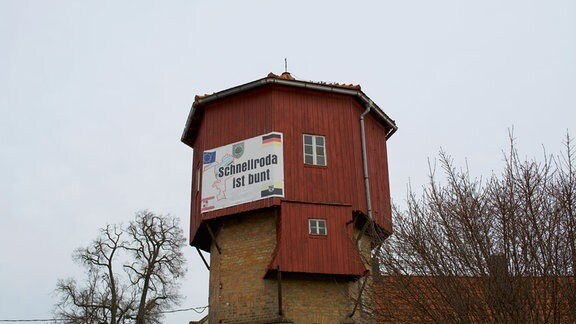 An einem Holzturm hängt ein Transparent mit der Aufschrift "Schnellroda ist bunt"