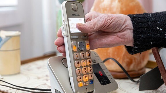Die Hand einer Seniorin greift zum Telefon.