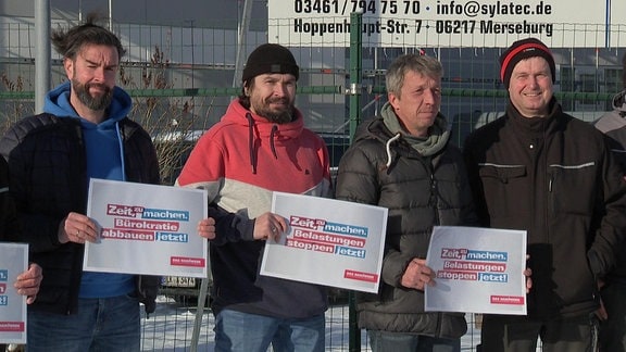 Mehrere Handwerker protestieren mit Transpareten vor einem Firmengelände in Merseburg.