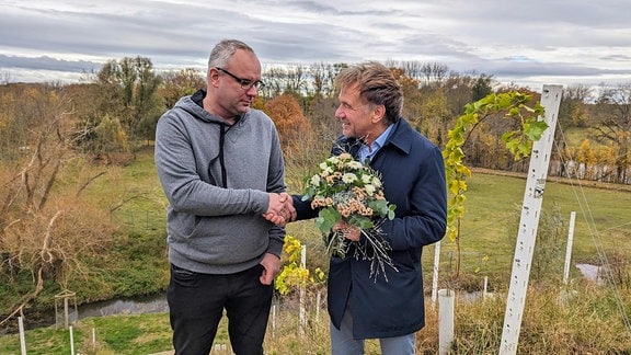Zwei Männer, einer mit einem Blumenstrauß