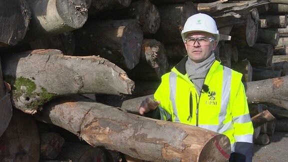 Mann mit Bauhelm, Warnweste und Schutzbrille hält einen Holzscheit.