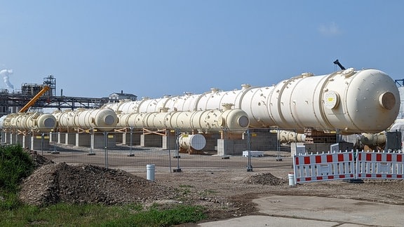 Blick auf mehrere große Rohre, die auf dem Gelände einer Raffinerie liegen.