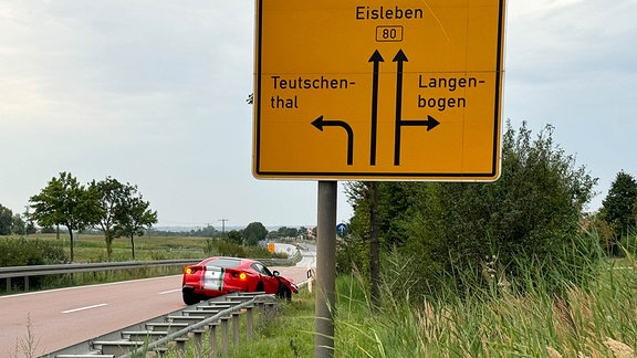 Rotes Auto steht hinter einem Verkehrsschild.